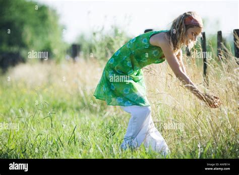 Young Woman Bending Over To Touch Tall Grass In Rural Field Stock Photo