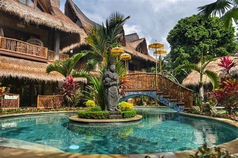 An Outdoor Swimming Pool Surrounded By Palm Trees And Thatched Roof Houses With Balconies