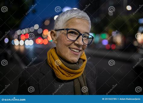 Smiling Mature Senior Woman With Short Gray Hair And Eyeglasses Walking On Street Night Scene