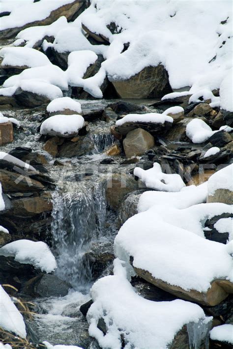Snow Covered Rocks Beside A Mountain Stream In The French Alps