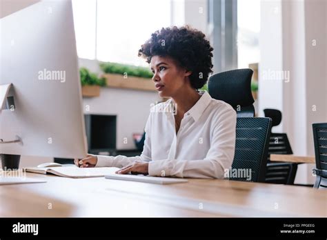 Jeune femme africaine assise à son bureau à la recherche à l écran de l