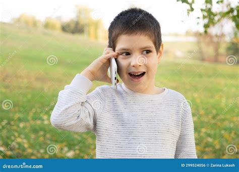Handsome 6 Year Old Boy Talking On The Phone While Standing In Park In