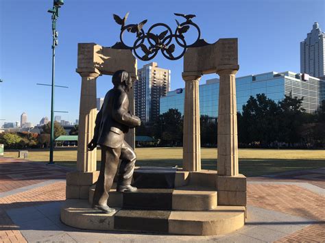 A Statue Of A Man Holding A Tennis Racquet In Front Of The Olympic Rings