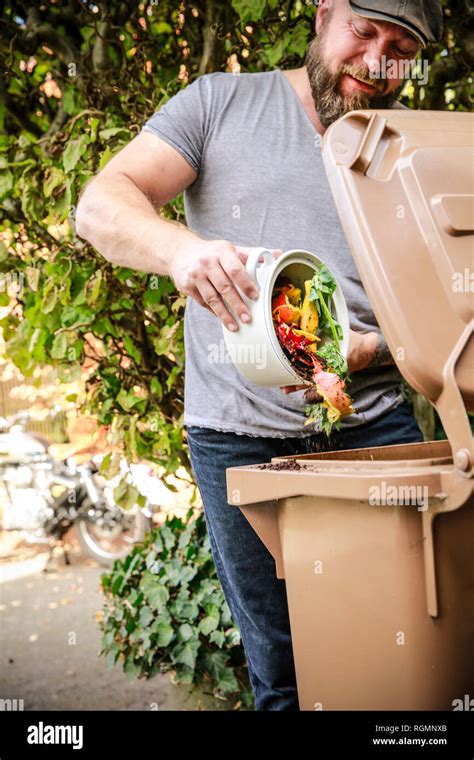 Mature Man Throwing Kitchen Scraps Into Bio Waste Container Hi Res