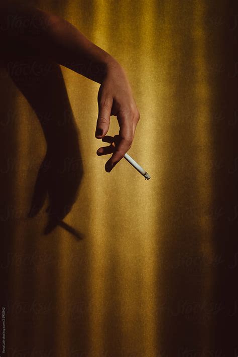 Womans Hand Holding A Cigarette On A Golden Background By Stocksy