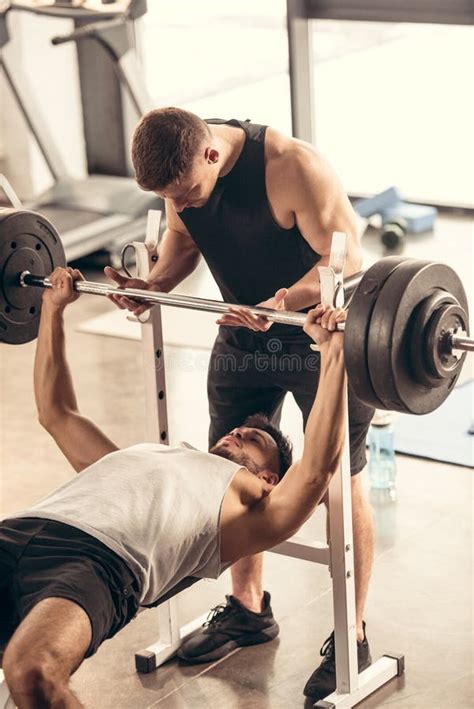 Muscular Trainer Helping Sportsman Lifting Barbell With Heavy Weights