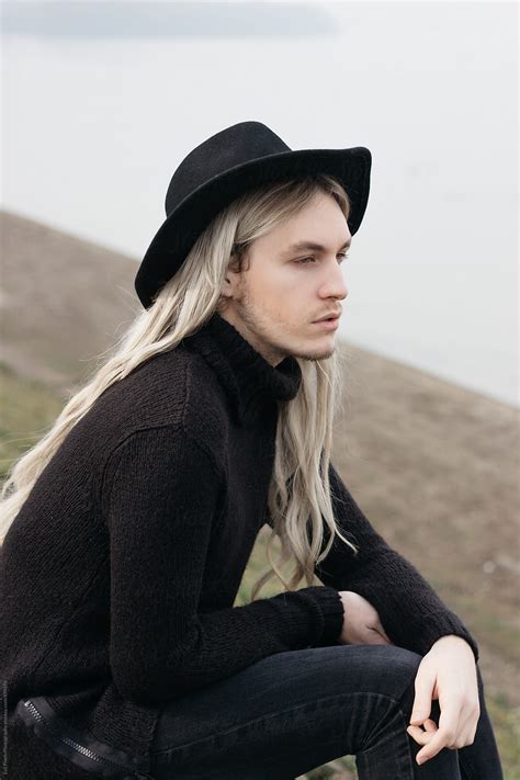 portrait of a male model with long hair and black hat sitting near