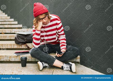 Concerned Student Girl In Striped Outfit And Glasses Sits Outside With