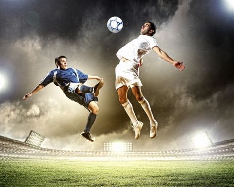 Two Football Players In Jump To Strike The Ball At The Stadium Stock