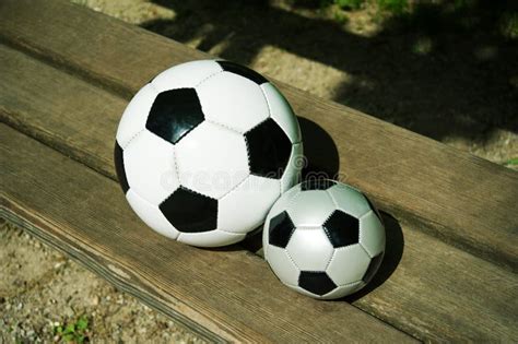 Two Soccer Balls One Big One Small Are Laying Together On A Park