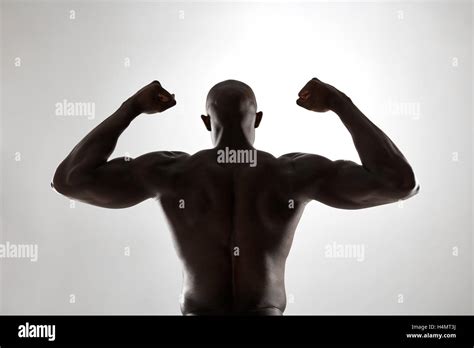 Strong Back Of A Black Muscular Man Flexing His Arms Against Grey