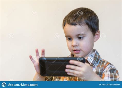 Portrait Of A Smiling Little Boy Holding Mobile Phone Over Light