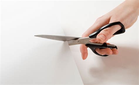 Close Up Of Hand Holding Scissors And Cutting Through Paper Stock Photo
