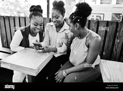 Three African American Girls Sitting On The Table Of Caffe And Looking On Mobile Phone Stock
