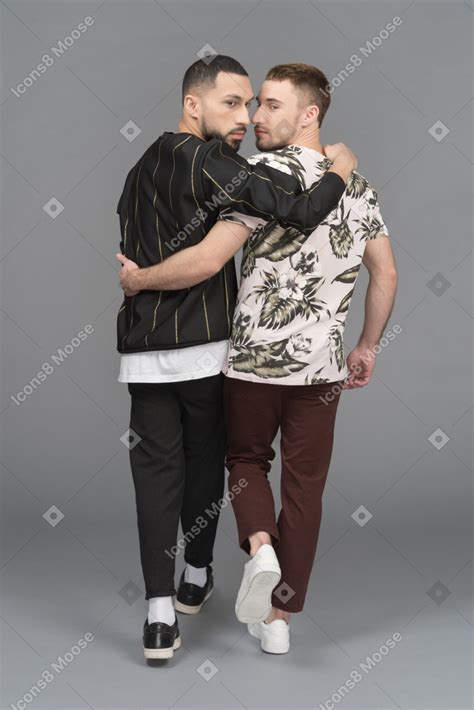 Back View Of Two Young Men Walking Forward And Half Hugging While
