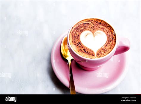Pastel pink cappuccino cup with heart latte art. Coffee on the marble