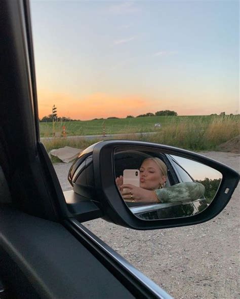 A Woman Taking A Selfie In The Side Mirror Of A Car With Her Cell Phone