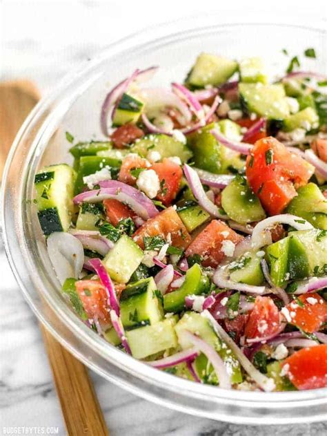 A Glass Bowl Filled With Cucumber Onion And Tomato Salad On Top Of A