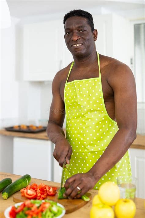 Smiling Half Naked Man In Yellow Apron Cooking Vegetable Salad In Home Kitchen Stock Photo