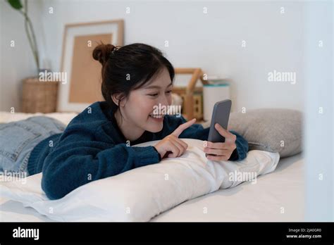 Beautiful Asian Woman Laying Down On White Bed Using Mobile Phone And Smile In Morning Sunday