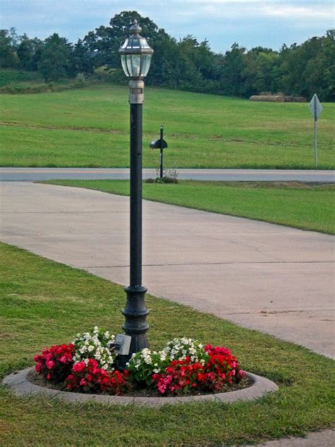 A Lamp Post With Flowers Around It In The Middle Of A Sidewalk And