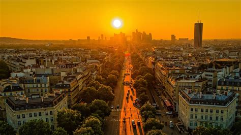 The Sun Is Setting Over An Urban Area With Tall Buildings And Trees In