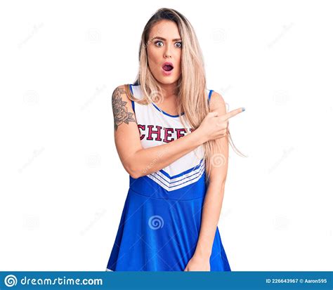 Young Beautiful Blonde Woman Wearing Cheerleader Uniform Surprised Pointing With Finger To The