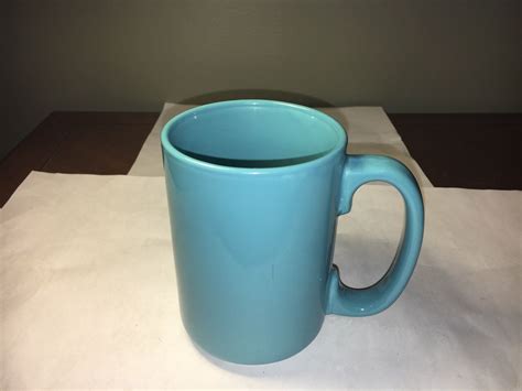 A Blue Coffee Mug Sitting On Top Of A White Table Cloth Next To A Wall