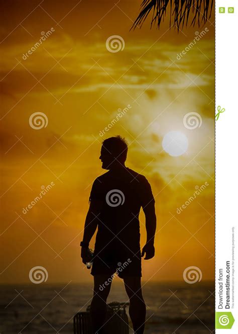 Silhouette Of Man Standing On The Beach With Water Bottle Stock Photo