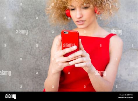 Latin Young Woman With Curly Blonde Hair Watching Her Social Media On The Phone With Headphones