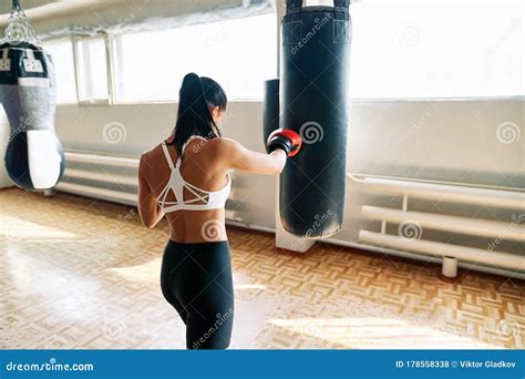 Back View Of Female Boxer Hitting A Huge Punching Bag At Fitness Gym