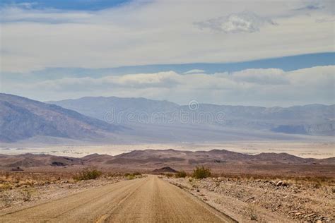 Open Desert Road In Death Valley Leading To Large Mountains And Sandy