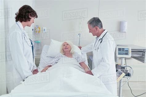 Two Doctors Talking To Senior Female Patient In Hospital Bed Stock
