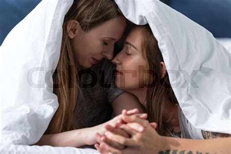 Two Happy Lesbians Holding Hands While Lying Under Blanket On Bed