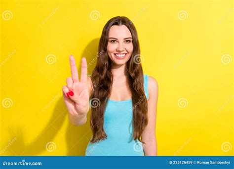 portrait of attractive cheerful girl showing giving v sign good mood over bright yellow color