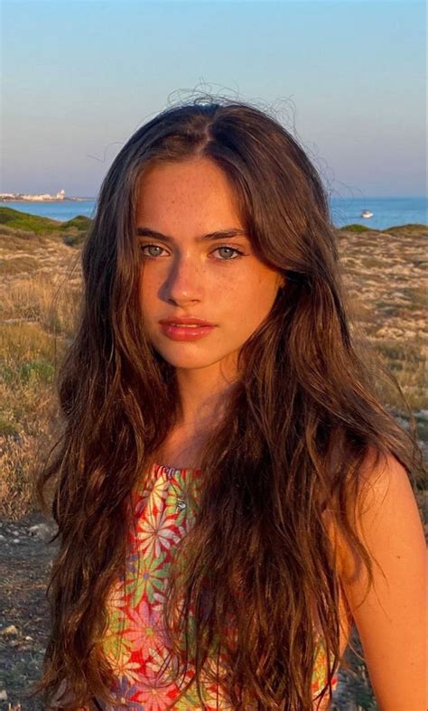 A Woman With Long Brown Hair Standing In Front Of The Ocean And Looking