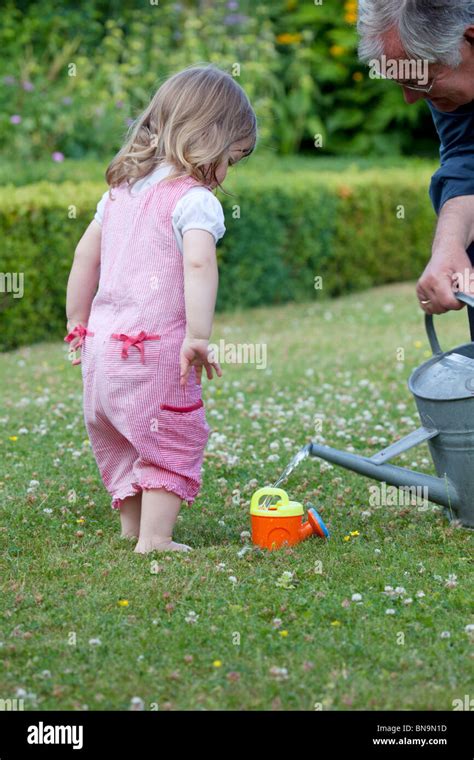 2yr Old Girl Waiting For Grandfather To Fill Up Her Watering Can Stock