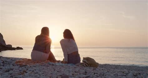 Two Women Sitting On Beach Watching Sunset Best Friends Enjoying A Relaxing Summer Vacation At