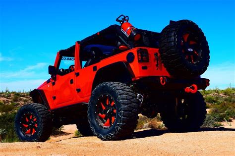An Orange Jeep With Black Tires And Red Rims In The Desert On A Sunny Day
