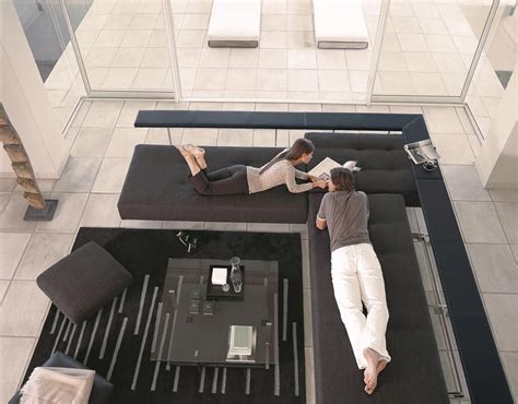 A Man Laying On Top Of A Black Couch Next To A Woman In White Pants