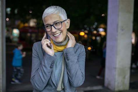 Smiling Mature Senior Woman With Short Gray Hair And Eyeglasses Use Phone On Street Night Scene