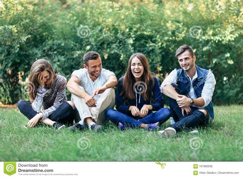 Funny Laughing Friends Sitting On Grass With Crossed Legs Stock Photo
