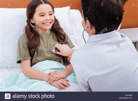 Back View Of Boy Doctor Checking Girl Patient With Stethoscope In