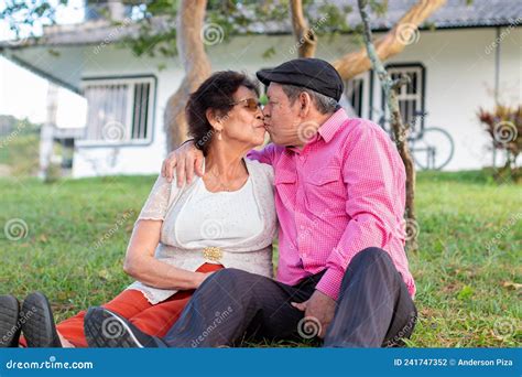 Cute Old Couple Sitting In A Garden Full Of Nature And Trees Giving Each Other A Romantic Kiss