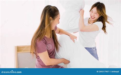 two happy and attractive asian women having a pillow fight with smiles laugh and fun together