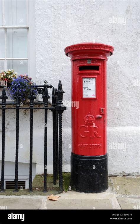 Traditional British Red Pillar Box Against Whitewashed Wall Stock Photo
