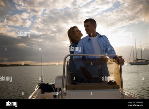mid adult woman with her arms around her mature husband as they cruise on a boat at sunset stock