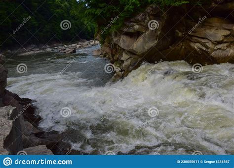 A Stormy Stream Of A Mountain River With A Waterfall Flows Between The