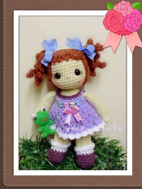 A Crocheted Doll With A Purple Dress And Blue Bow Holding A Green Frog