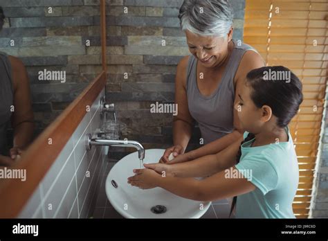 Grandmother And Granddaughter Washing Hands In Bathroom Sink At Home